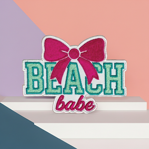 Embroidered patch with 'BEACH babe' text and pink bow on a colorful background