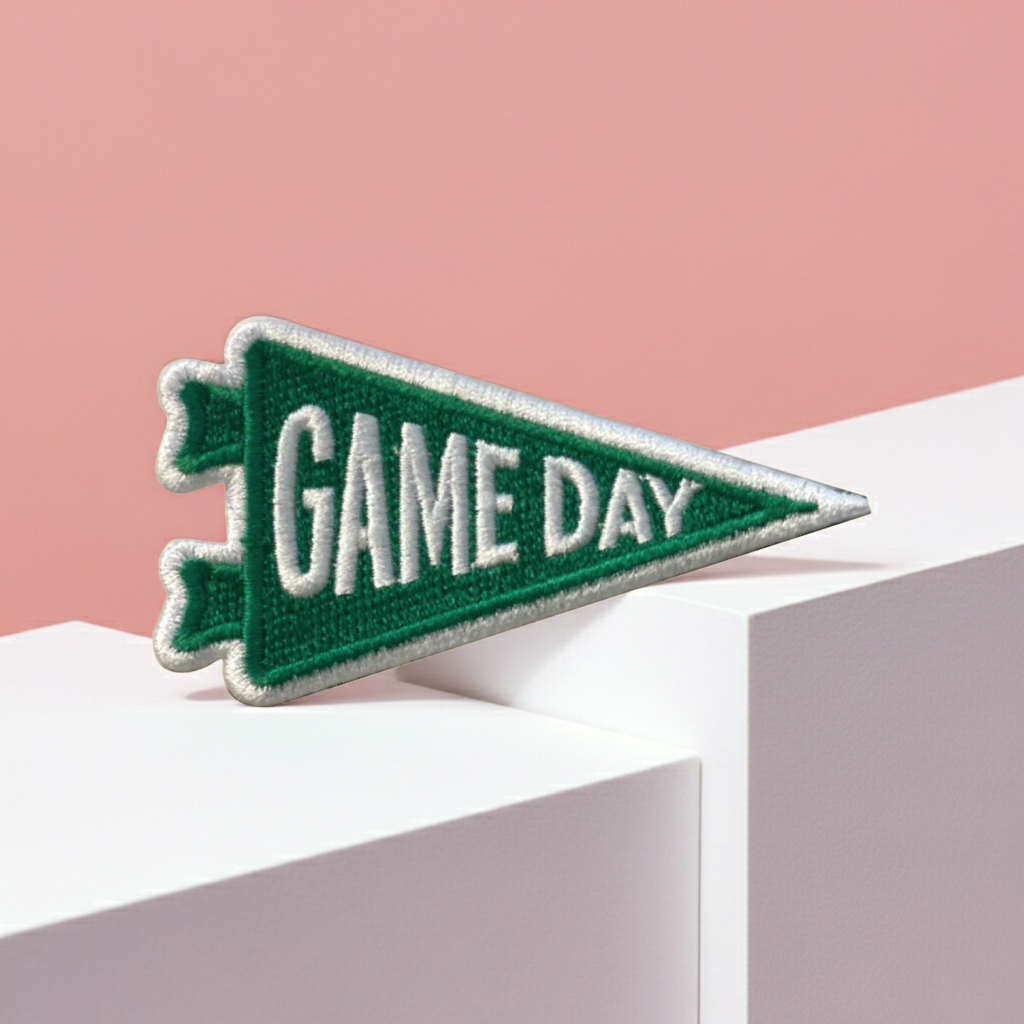 Green 'GAME DAY' pennant patch on a pink and white geometric background